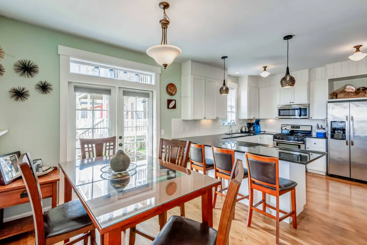 A bright and modern open-plan dining area with a large table surrounded by comfortable chairs, a nearby kitchen island, and a window streaming in natural light. Decorative touches and wall art add a homely charm.