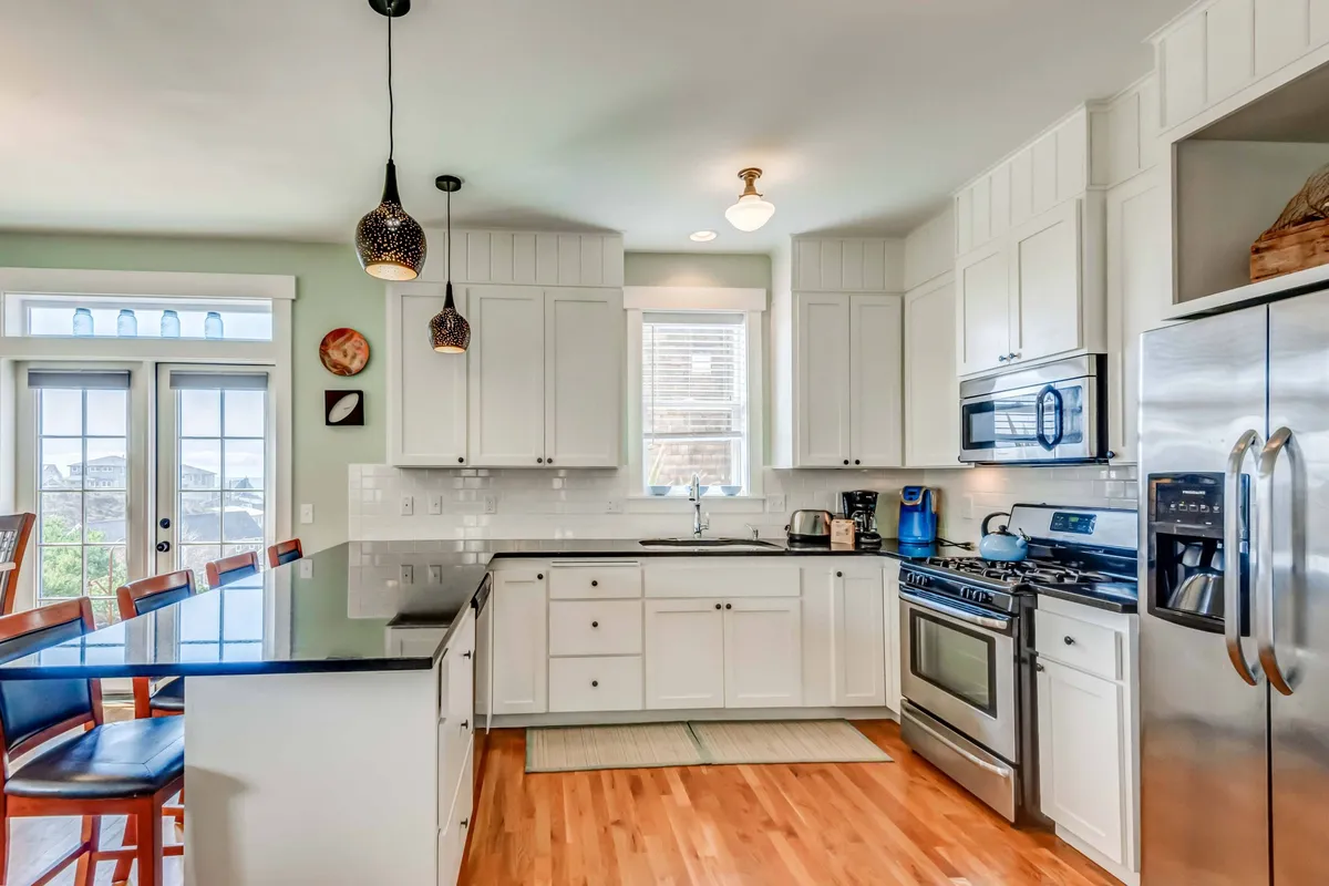A welcoming kitchen space featuring an island counter with bar stools, modern appliances, and abundant natural light from a large window. The bar seating encourages casual breakfasts and easy conversation.