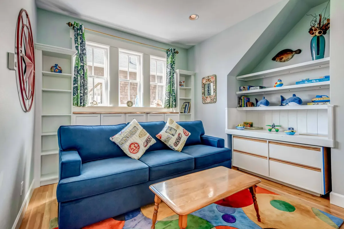 A cheerful, light-filled living room with a plush blue sofa accented by decorative pillows, a colorful area rug, and built-in shelves accessorized with personal touches. The setting feels lively and comfortable, ideal for socializing or relaxing between outdoor adventures.