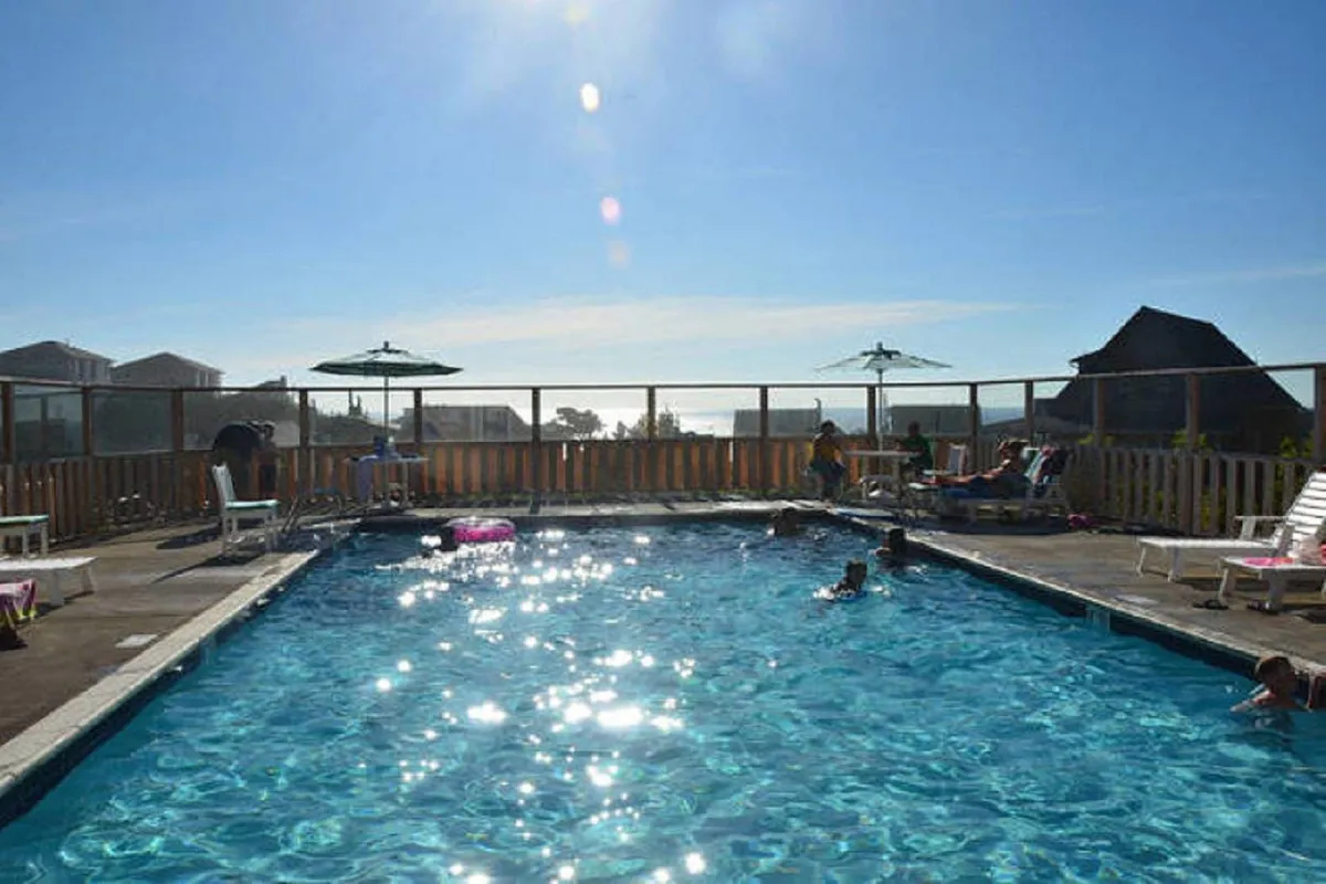 A close-up of the sparkling swimming pool, featuring poolside loungers, umbrellas, and sunlight dancing on the water. The mood is playful and carefree, emphasizing relaxation and summer fun.