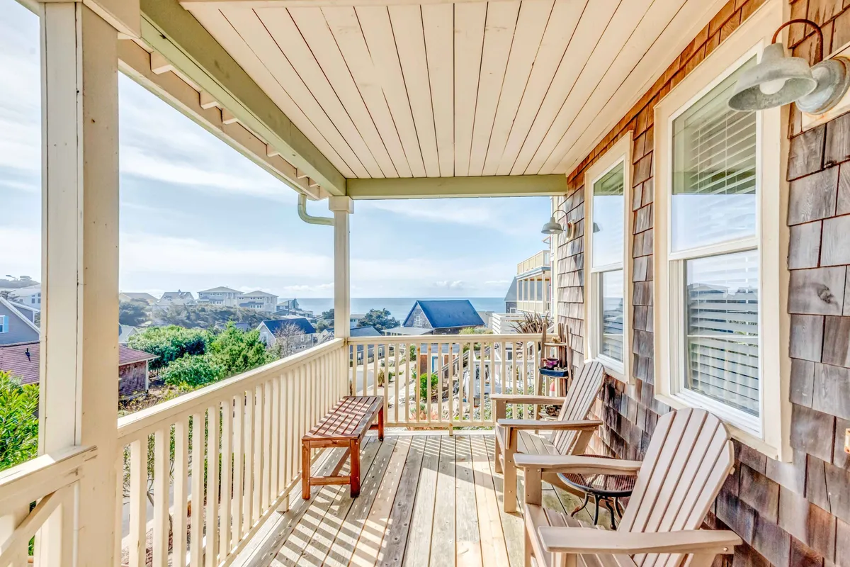 A serene wooden deck overlooks the ocean, furnished with Adirondack chairs and a wooden bench. The space exudes a peaceful, coastal vibe, perfect for lounging, reading, or socializing while taking in the views and sunsets.