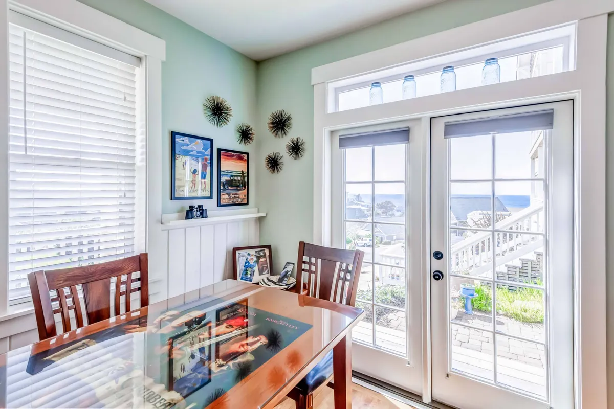 This bright dining area features a large table set against double doors that likely open to the outdoors. Sunlight streams through the glass, offering glimpses beyond the interior, hinting at easy access to the exterior spaces perfect for pet-friendly adventures. The cheerful decor and inviting atmosphere set the stage for shared meals before or after exploring the beaches and neighborhood with your furry companion.