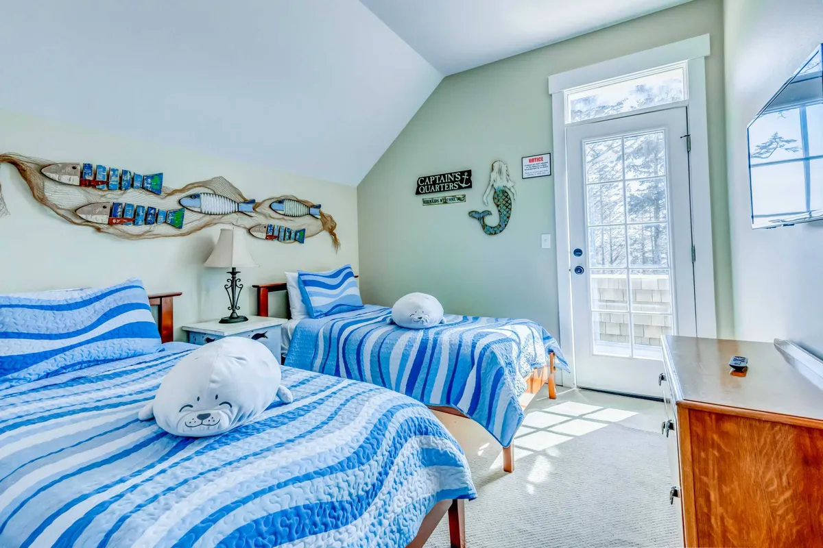 A playful bedroom with a bed dressed in striped bedding, decorative fish art above the headboard, a wooden dresser, and a glass door that lets in natural light. The room is cheerful and welcoming, perfect for children or guests.
