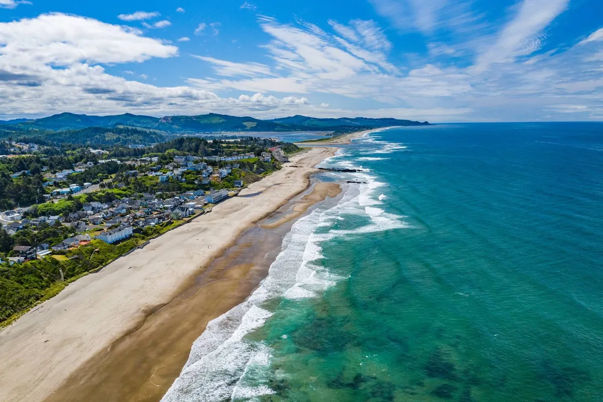 A sweeping view of the expansive beach and clear blue ocean along the Olivia Beach coastline, with a coastal town in the distance. The scene is tranquil, inviting beachcombing, water sports, and sunset watching.